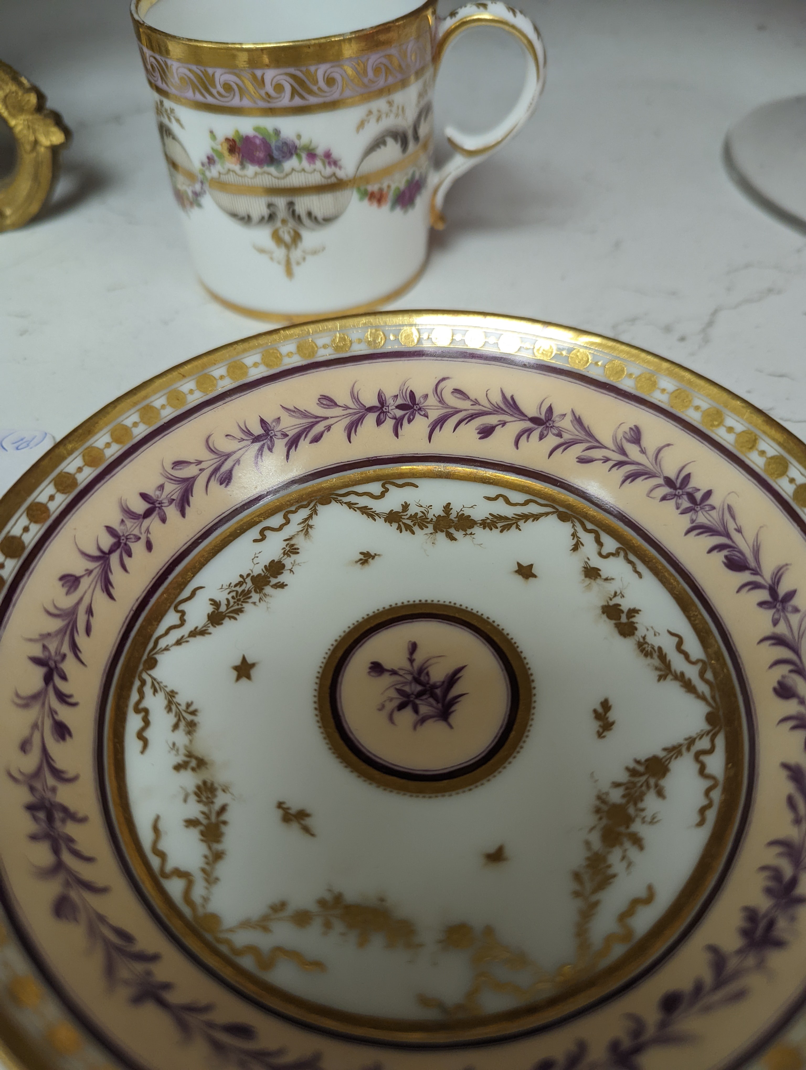 A Duc d'Angouleme coffee can and saucer painted with a puce chain of leaves on a salmon coloured ground and another painted with a flower chain, black feather and a gilt line, latter with stencilled red mark 'Manuf de M
